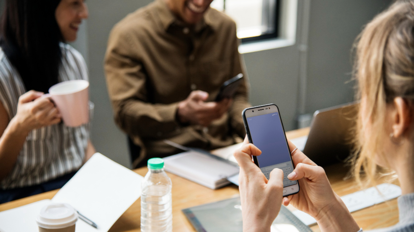 Colaboradores utilizando aplicativo de comunicação interna em smartphones durante reunião de equipe no ambiente corporativo.