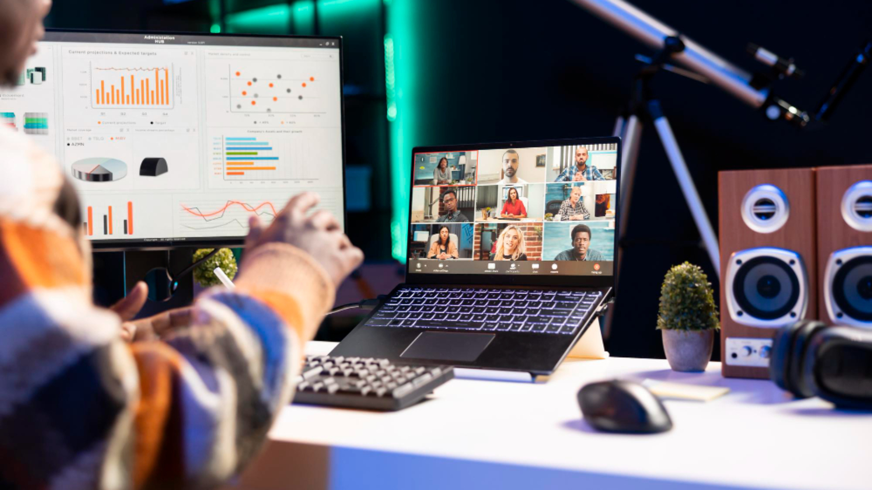 Profissional participando de uma videoconferência em um notebook enquanto acompanha dashboards de métricas em um monitor, representando o uso de uma plataforma de comunicação interna.