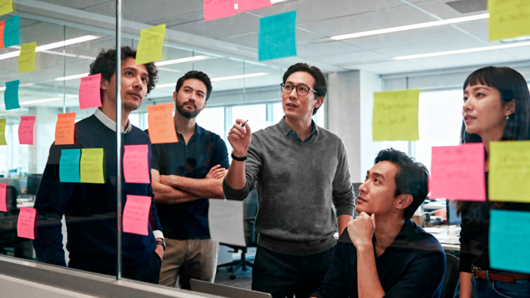 Equipe reunida diante de um quadro de vidro com post-its coloridos, discutindo ideias e estratégias para fortalecer a cultura organizacional e a marca empregadora.